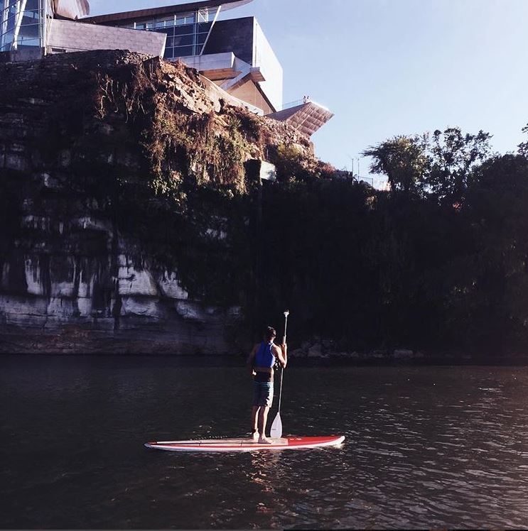 A person standing on a paddleboard near the bluff with the Hunter Museum above them.