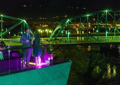 Two people stand on the Hunter Museum balcony at night with the pedestrian bridge and city in the background.