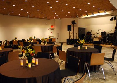 Tables set with black tablecloths and flowers. There is a stage in the front of the room.