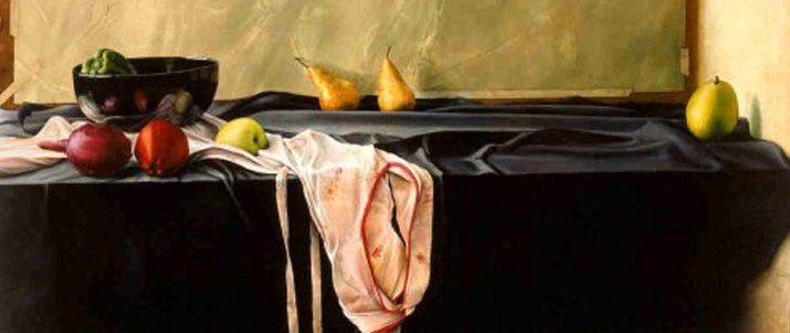 A table with a black tablecloth and fruit on it. An apron hangs off the side of the table.