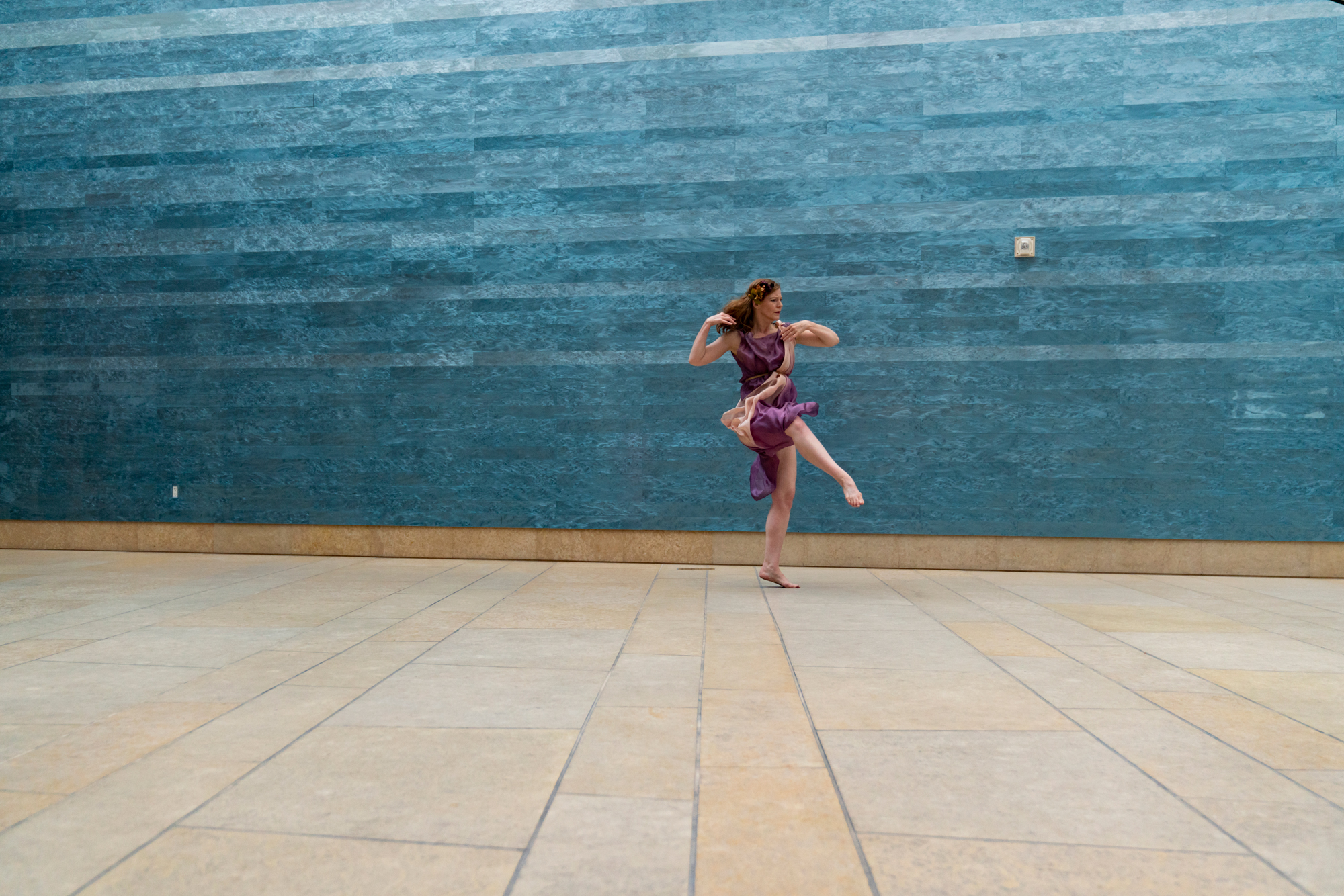 A dancer wearing a flowing purple dress is in the middle of a spin in front of a blue wall.