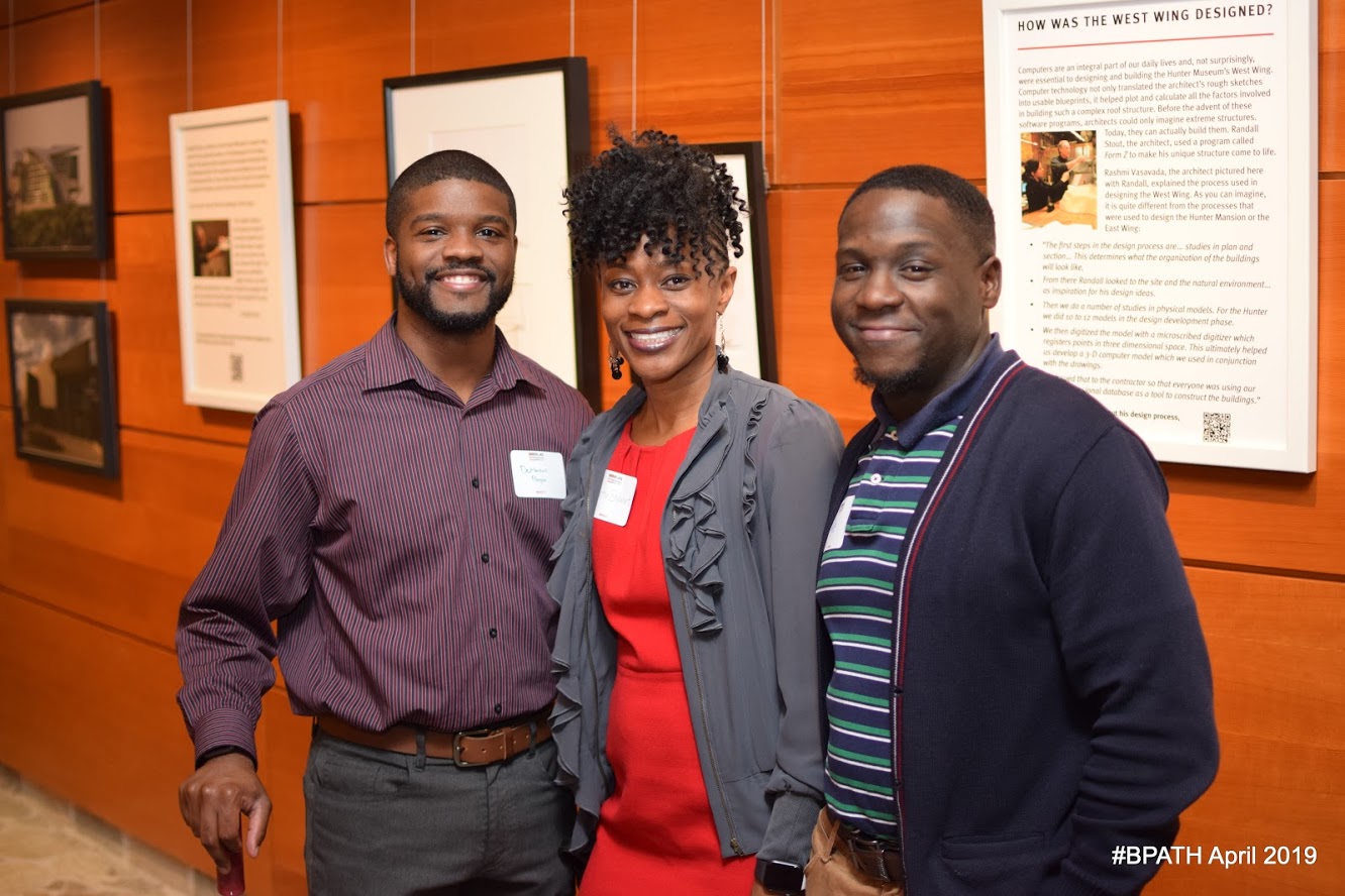 Three attendees of the Black Professionals at the Hunter event posed in front of the wall that depicts the history of the museum.