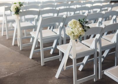 Rows of white chairs with a bouquet of white flowers on alternating rows.