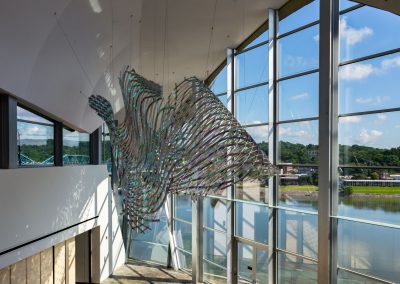 Weaved iridescent metal sculpture hanging from the ceiling in the lobby of the Hunter Museum with windows looking out to the river.