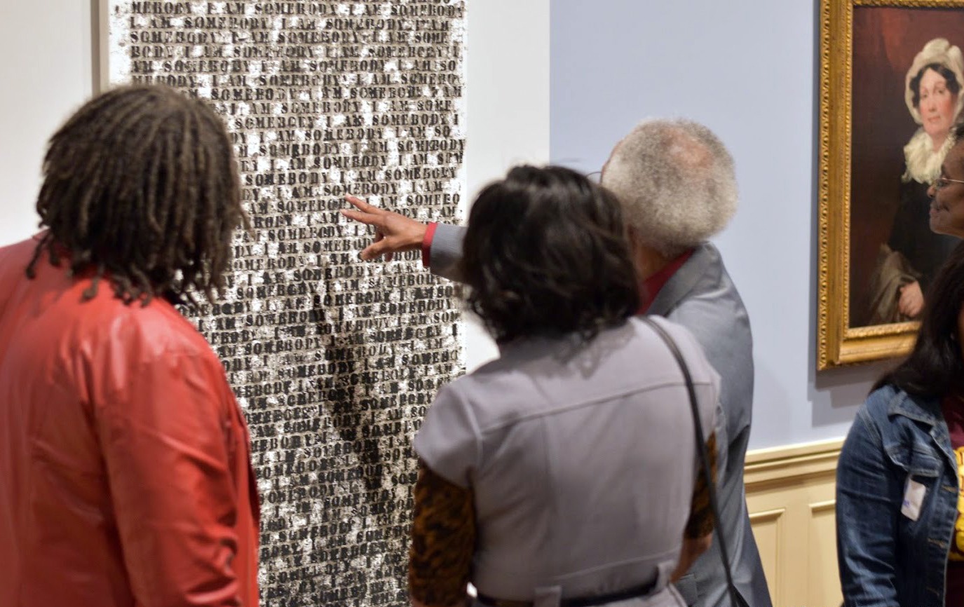 Three people examine and point at a painting by Glenn Ligon.