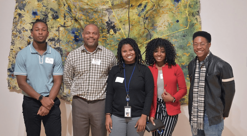 Group of five people attending Black Professionals at the Hunter standing in front of abstract art.